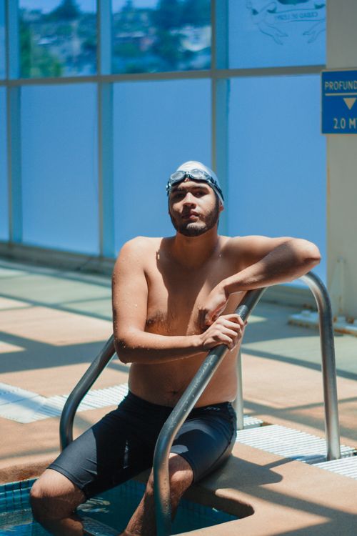 Free Man resting by poolside in indoor swimming area wearing swim gear, capturing relaxation and sport. Stock Photo