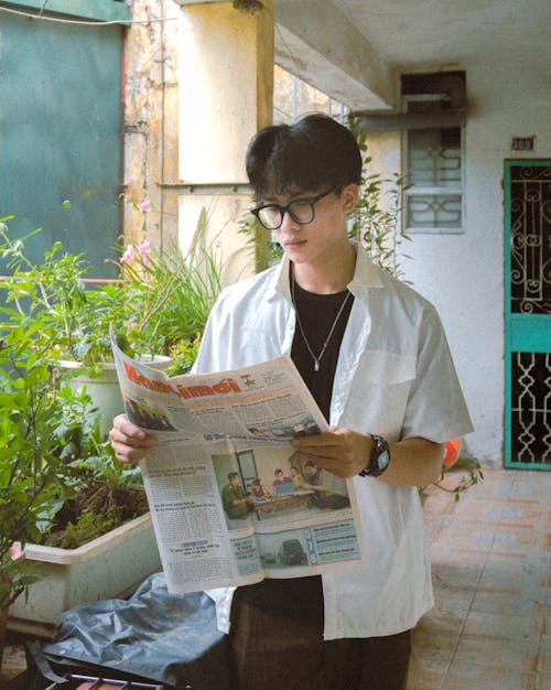 Young Brunette Man in White Shirt and Eyeglasses Reading a Newspaper