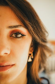 Artistic close-up of a young woman with makeup and earrings, highlighting her eye and facial details.