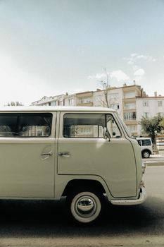 A classic light green vintage van parked on a city street with urban buildings in the background.