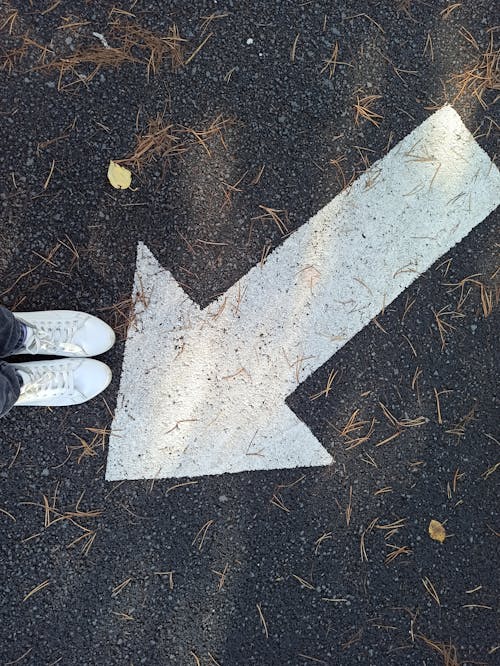 Top View of Legs in White Shoes, and an Arrow Sign on the Asphalt