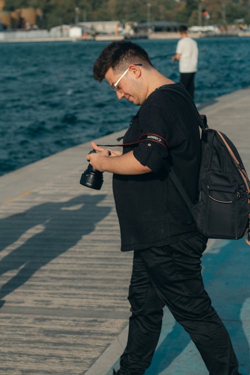 Photo of a Man Looking at a Digital Camera, Standing on a Pier