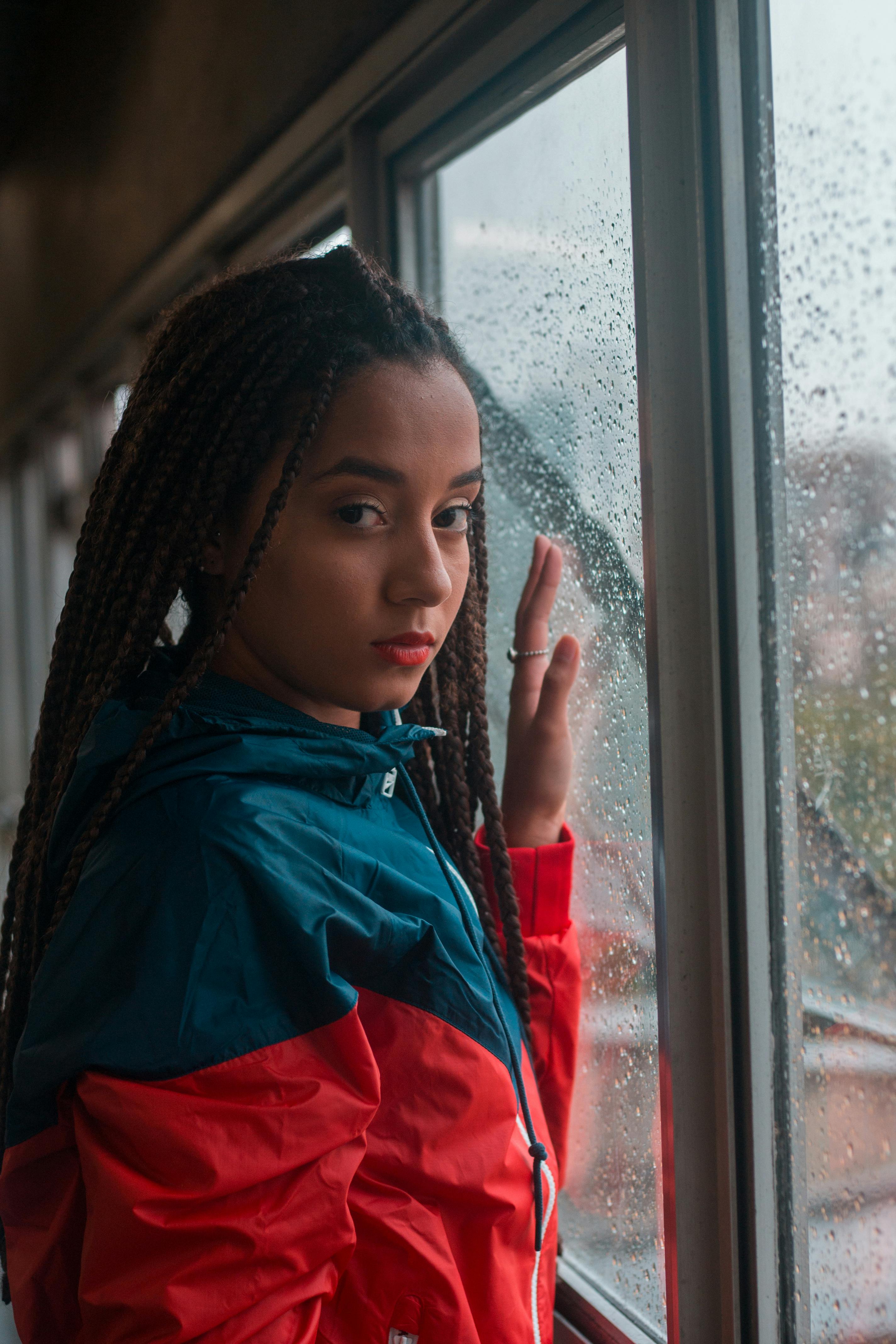 一位扎着辫子的年轻女子望着窗外的雨，肖像传达出体贴之情