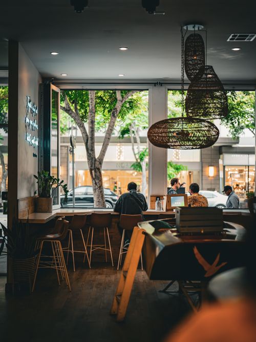 Free Chic urban café scene with patrons enjoying a relaxed atmosphere, modern decor, and warm lighting. Stock Photo