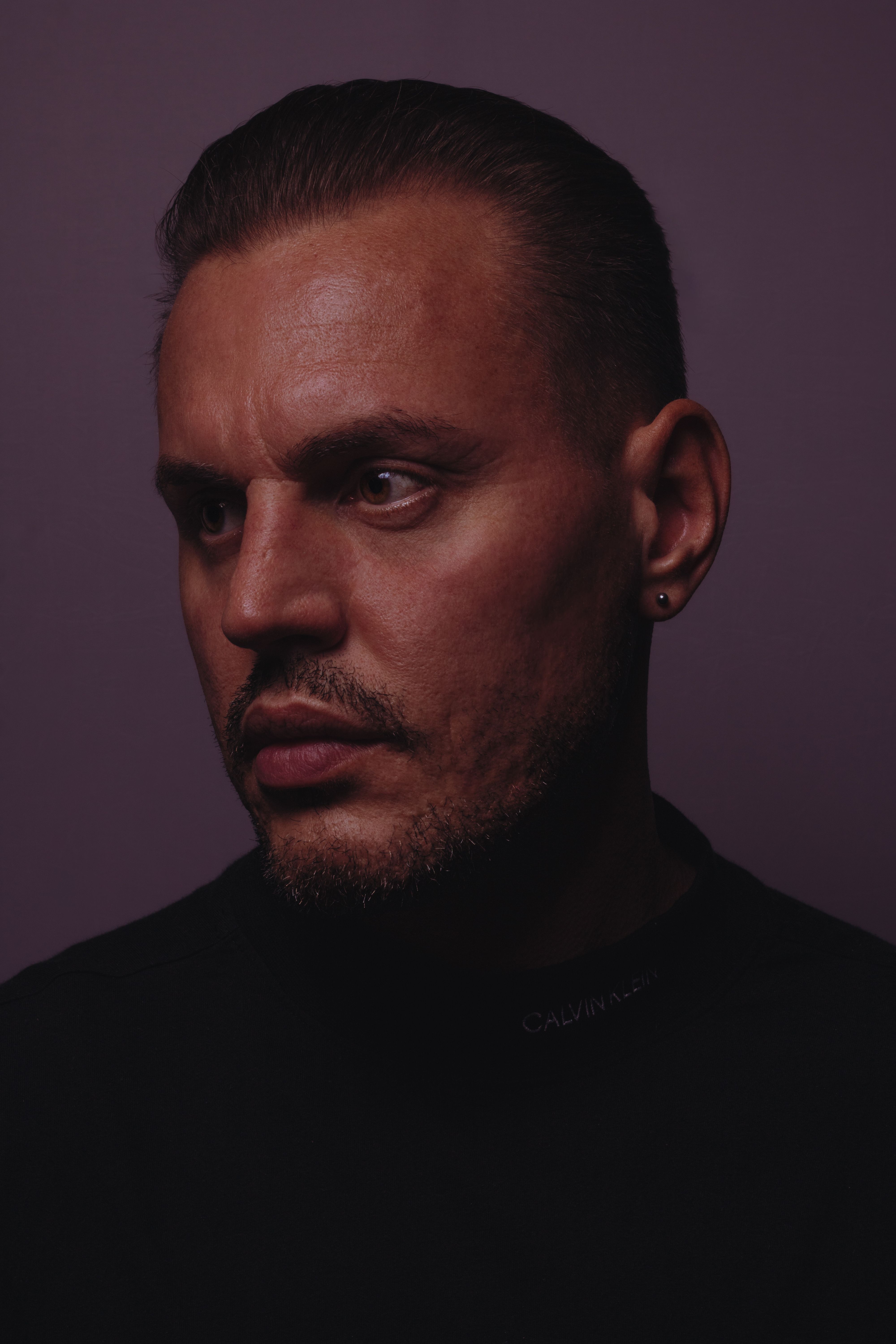 A moody and intense portrait of a man with stubble, captured in a studio setting.