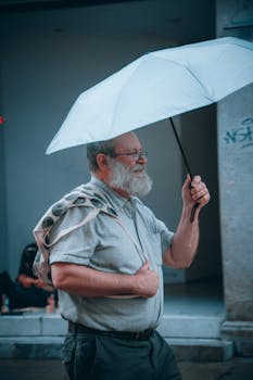 Senior man holding an umbrella, walking through urban Munich on a rainy day.