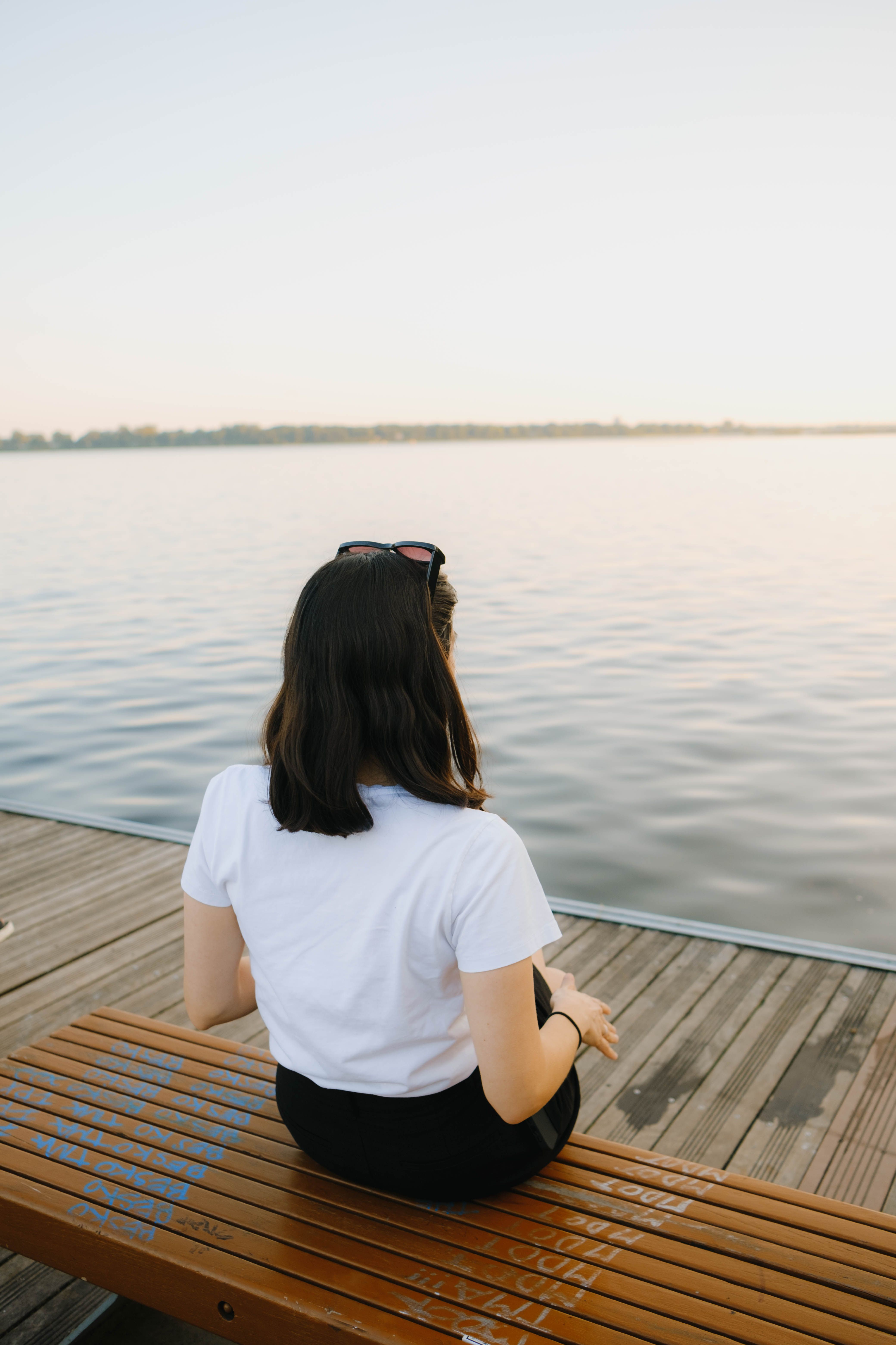 A woman sitting on a bench looking out at the water · Free Stock Photo