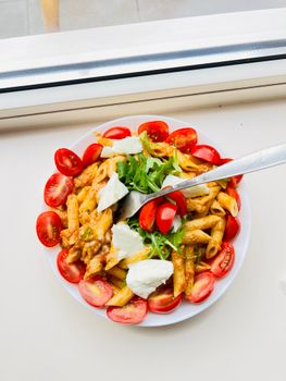 A vibrant plate of Italian pasta topped with fresh arugula, cherry tomatoes, and mozzarella.