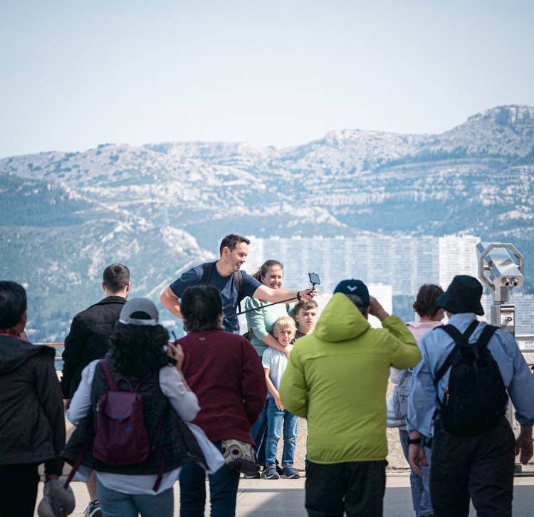 View Of People In A Crowd Taking A Selfie On The Background Of Mountains 