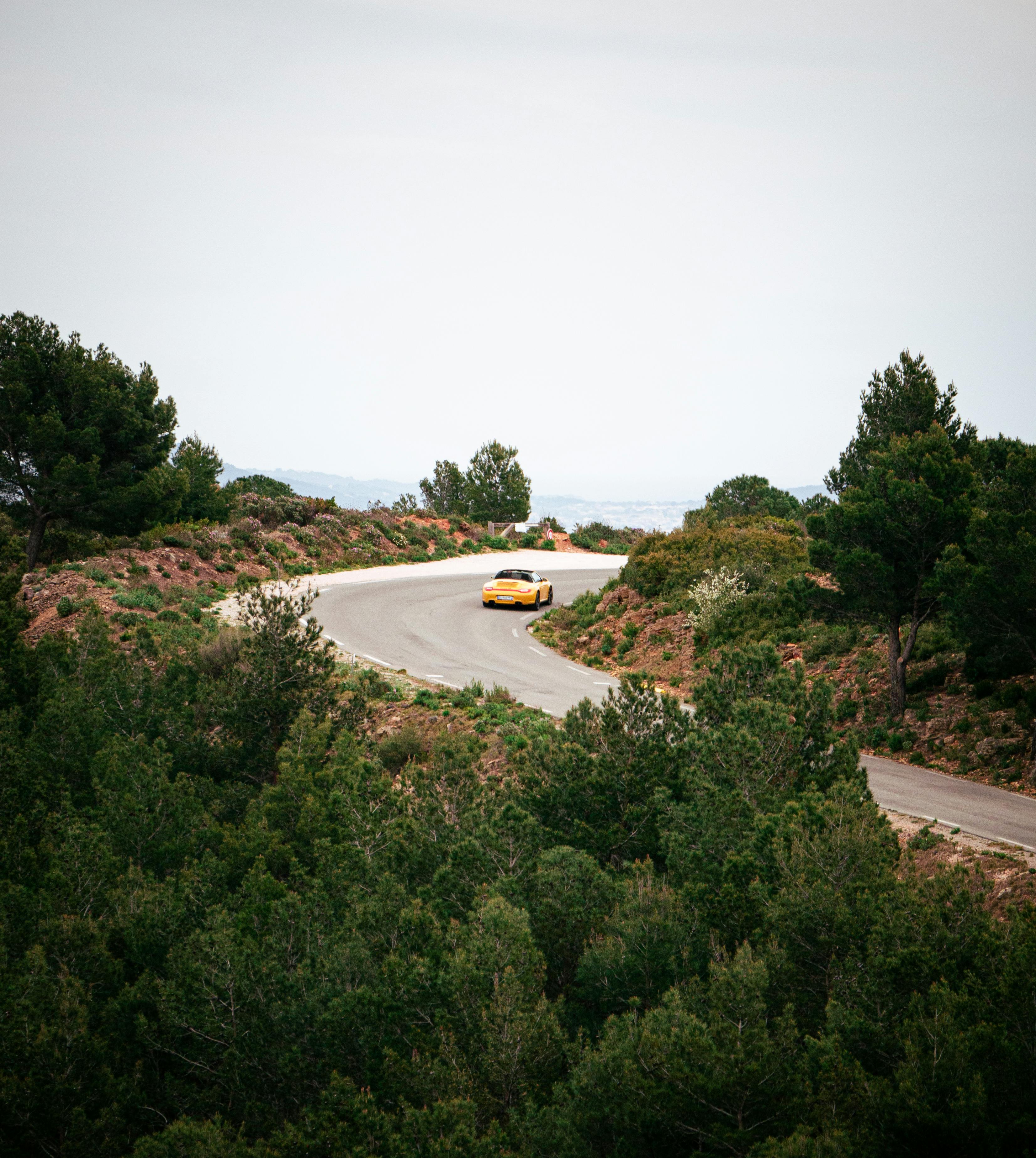 Yellow car navigating a winding road through lush, green mountain scenery.