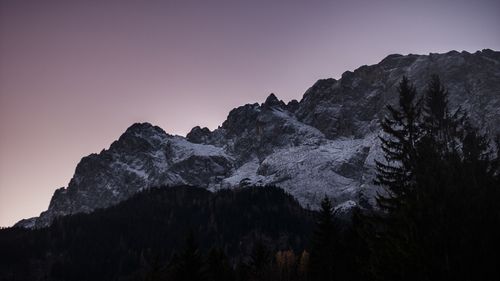 Free A breathtaking view of snow-covered mountains during twilight, surrounded by a forest. Stock Photo