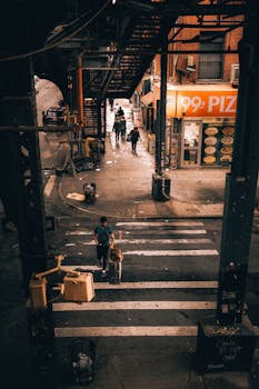 Busy street corner under an elevated train with pedestrians crossing in New York City.