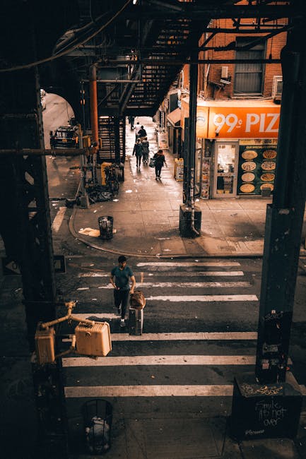 Busy street corner under an elevated train with pedestrians crossing in New York City.