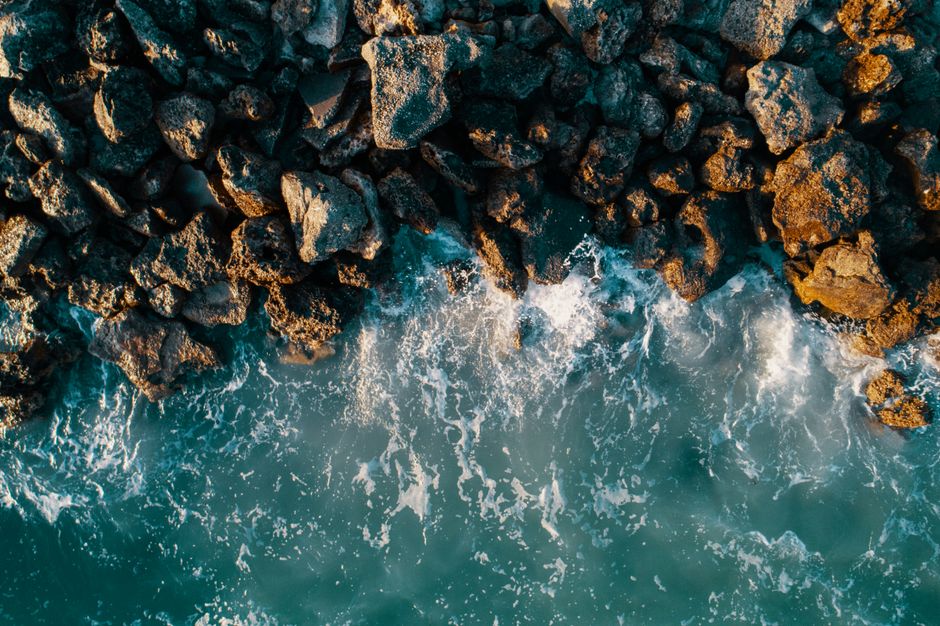 A stunning aerial view showcasing waves crashing against rocky seashore in a dynamic ocean landscape.