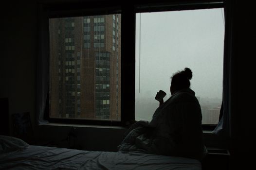 A woman sitting on a bed in front of a window