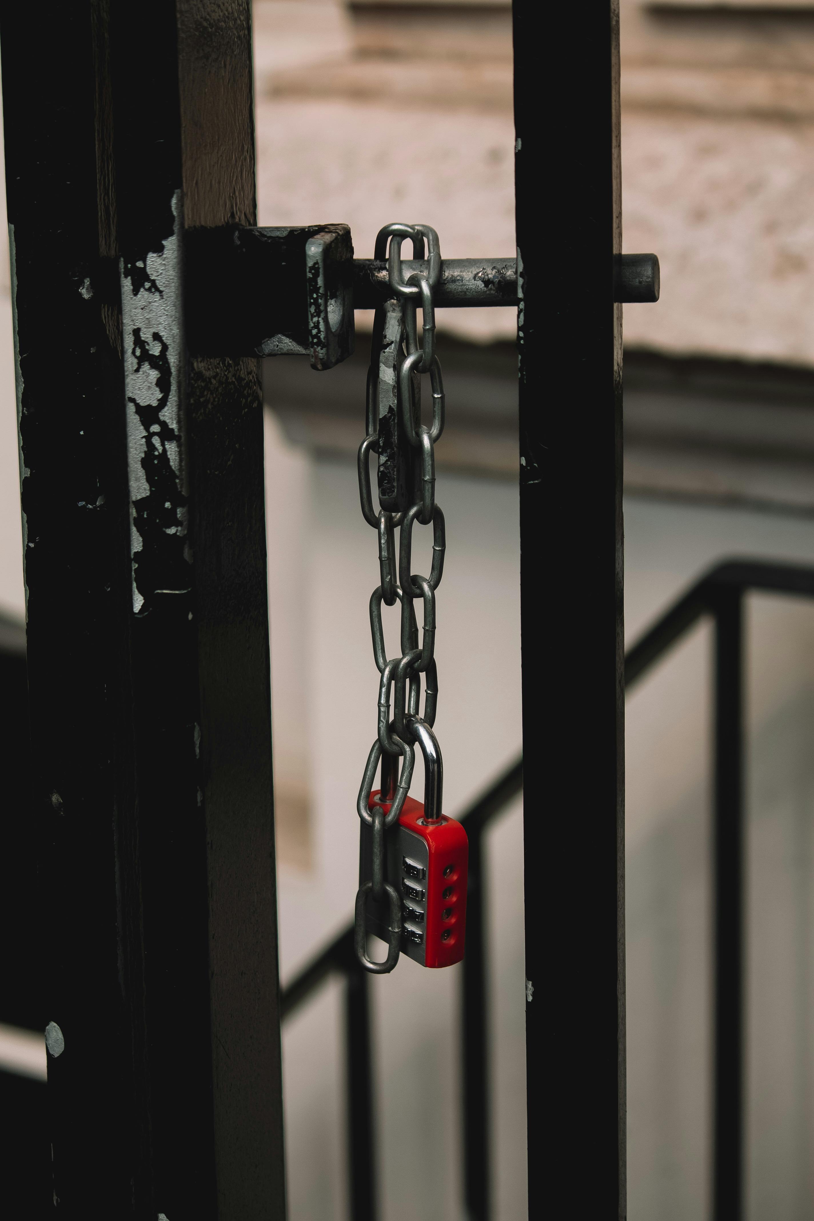 A secure red padlock with a chain on a black metal gate, photographed in London.