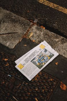 A newspaper lies on a fall city sidewalk surrounded by leaves, capturing urban life details.