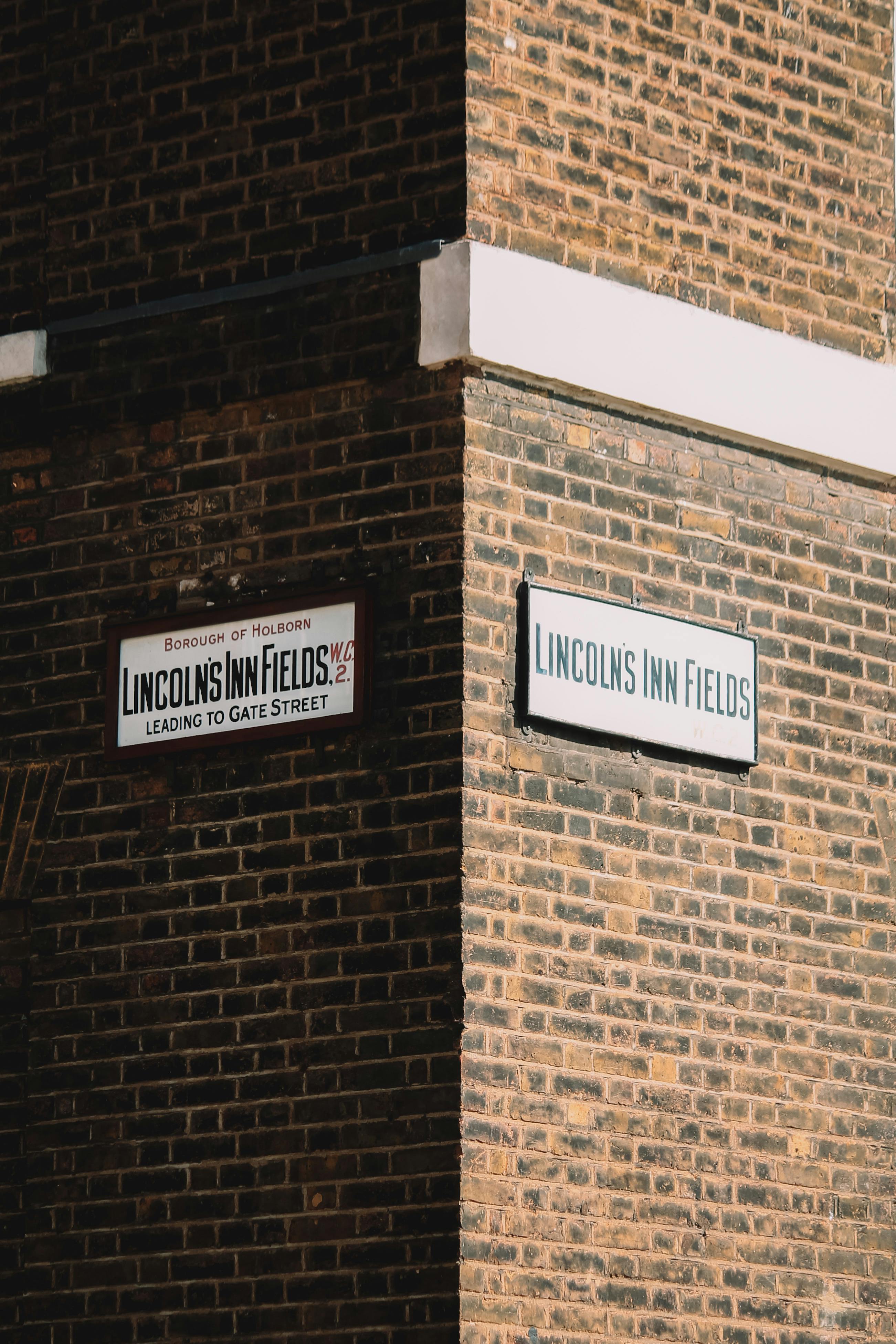 Close-up of Lincoln's Inn Fields street signs on a red brick building corner in an urban setting.