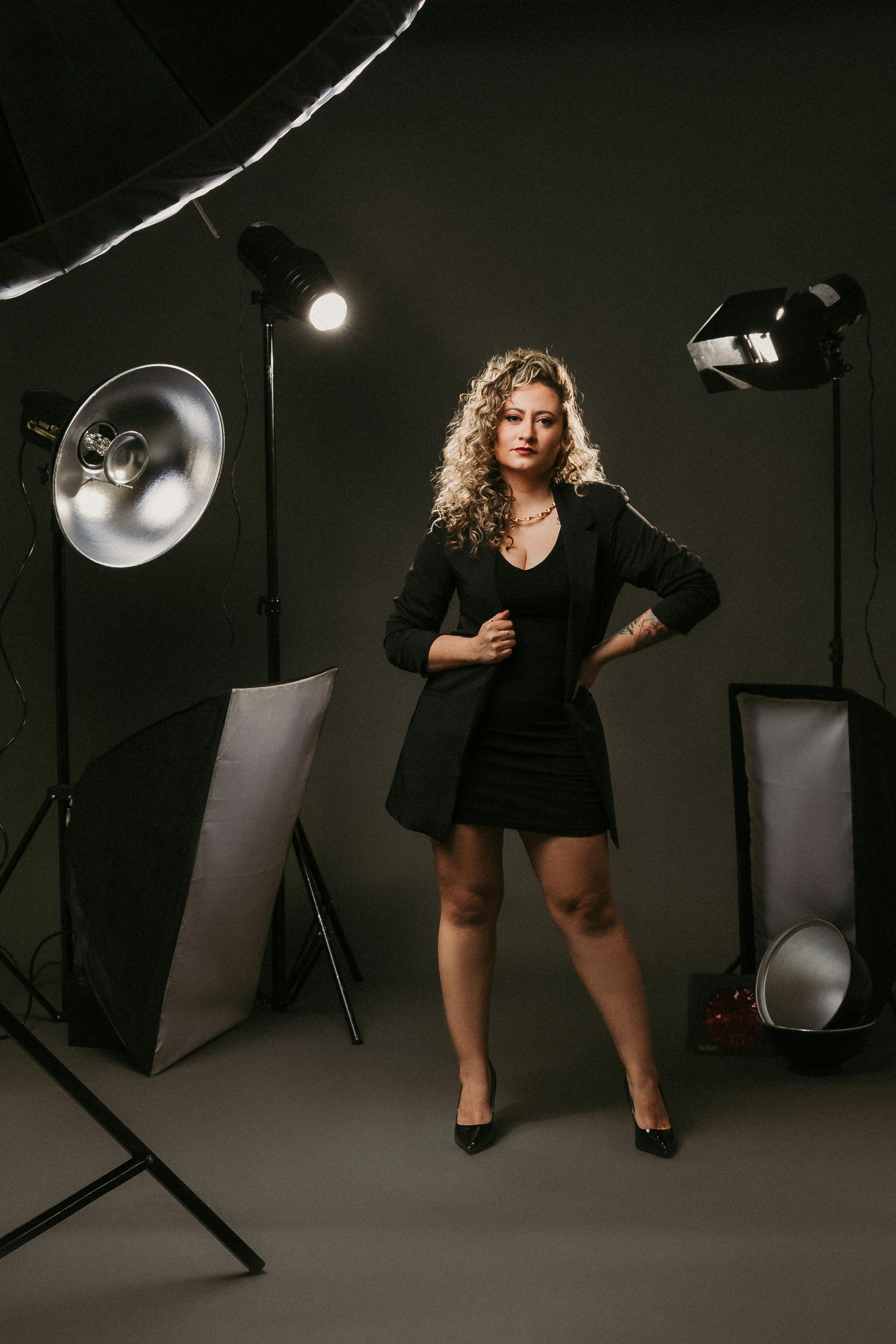 Gratis Wanita Mengenakan Mini Dress Hitam Dan Blazer Dikelilingi Peralatan Studio Foto Foto Stok