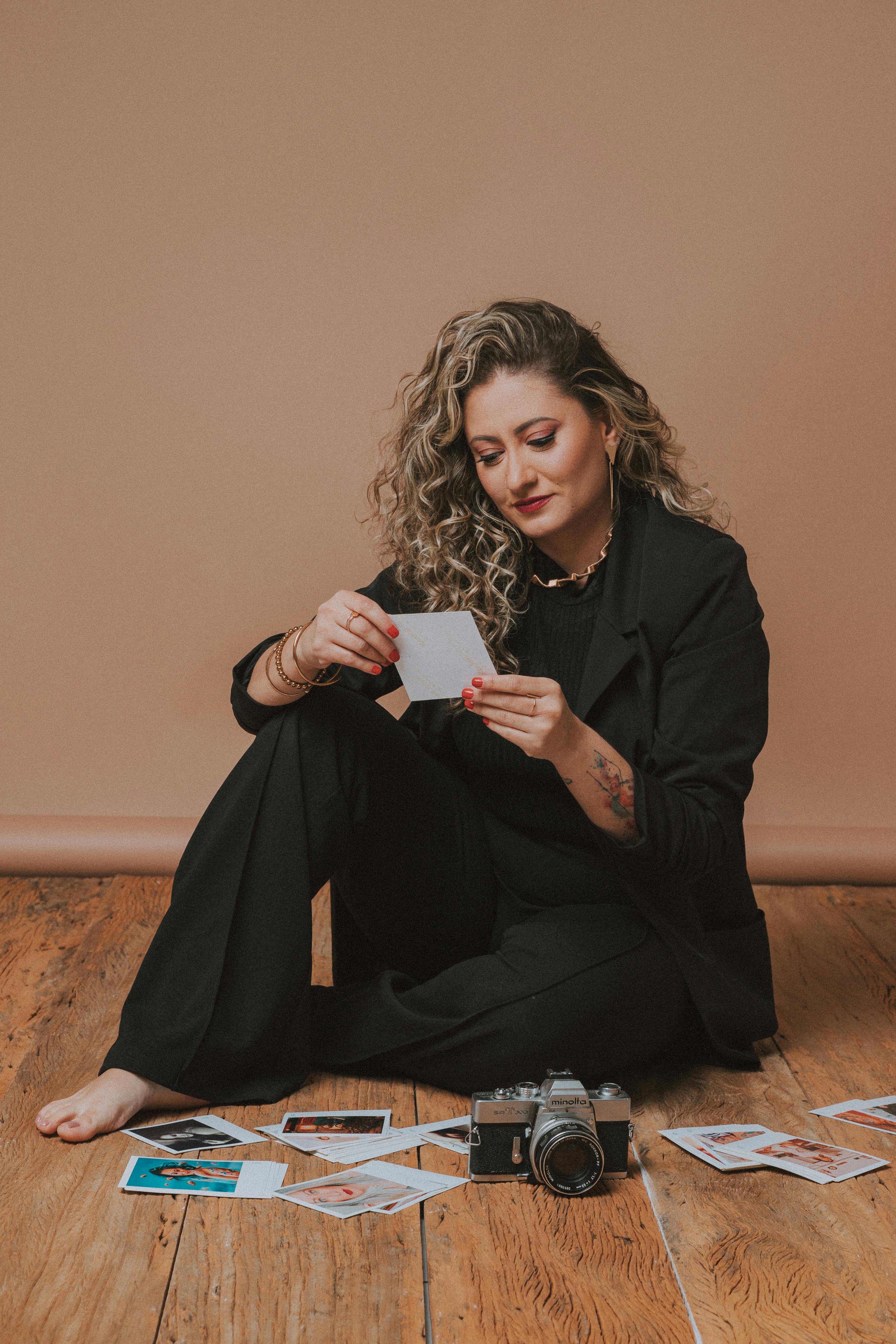 A woman reviews Polaroid photos while sitting on a wooden floor, with a vintage camera and casual attire.