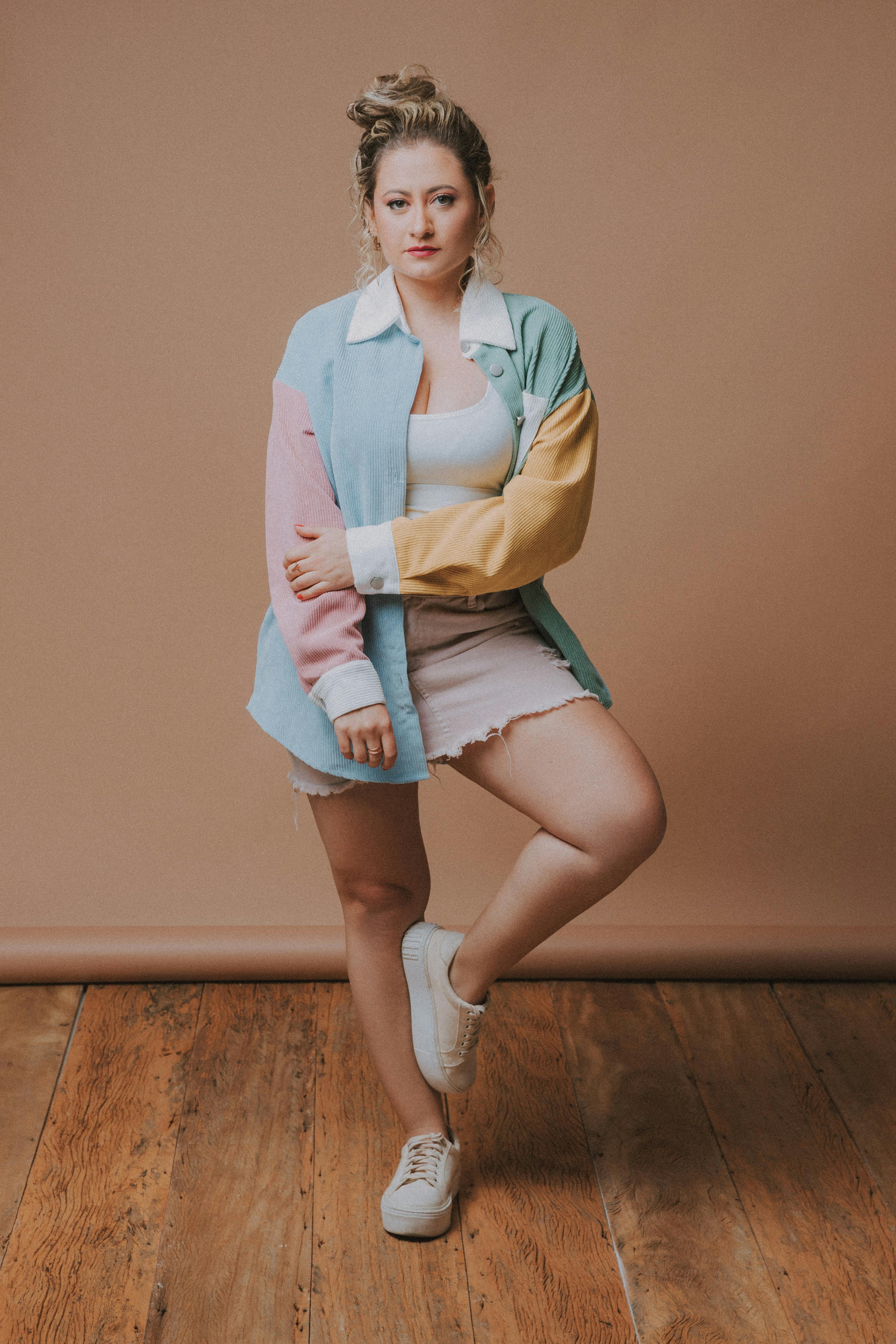 Woman posing in pastel jacket and mini skirt against brown background.