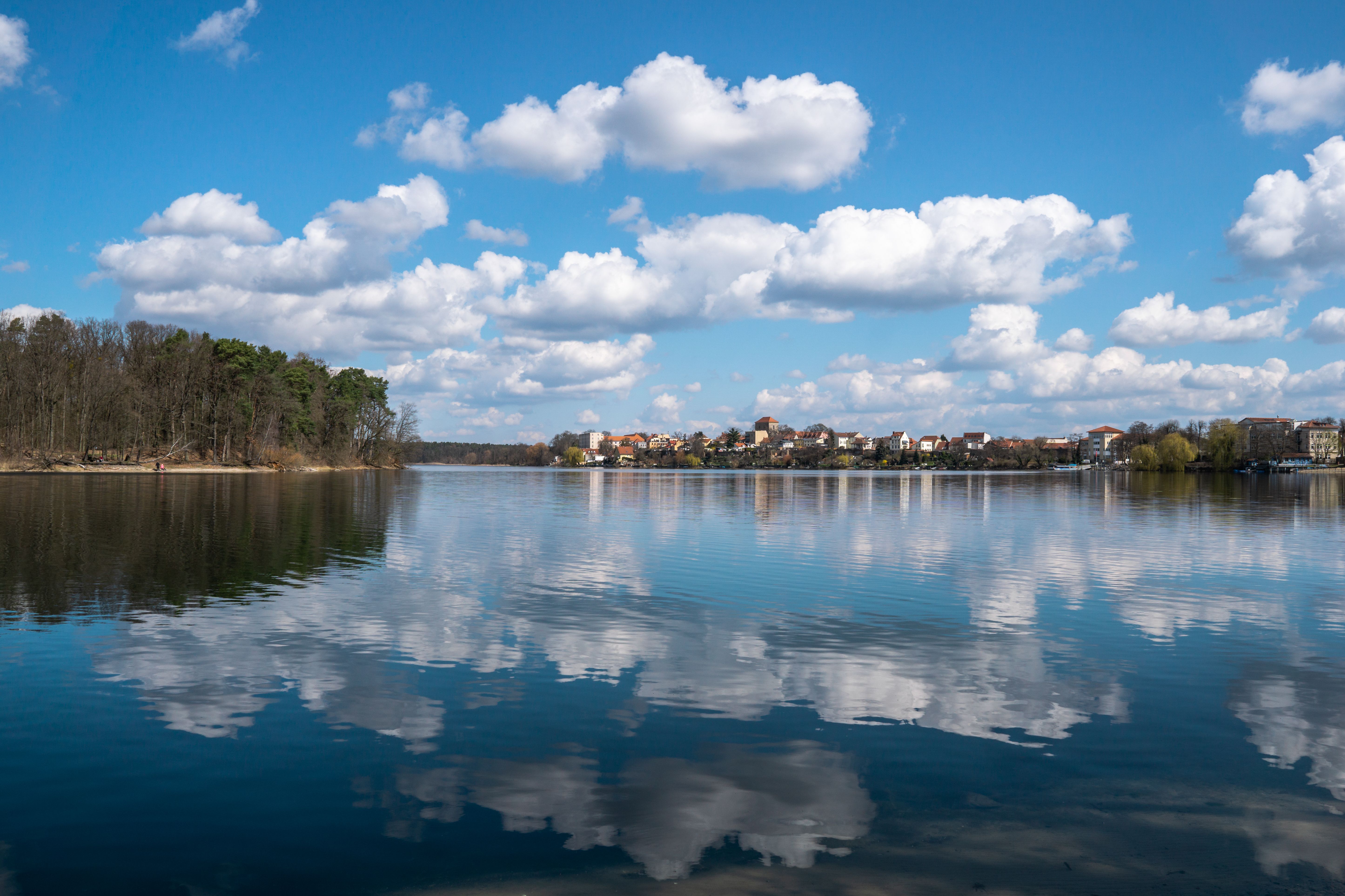 Stunning clouds reflect on Strausberg Lake with a scenic view of the nearby town and forest.