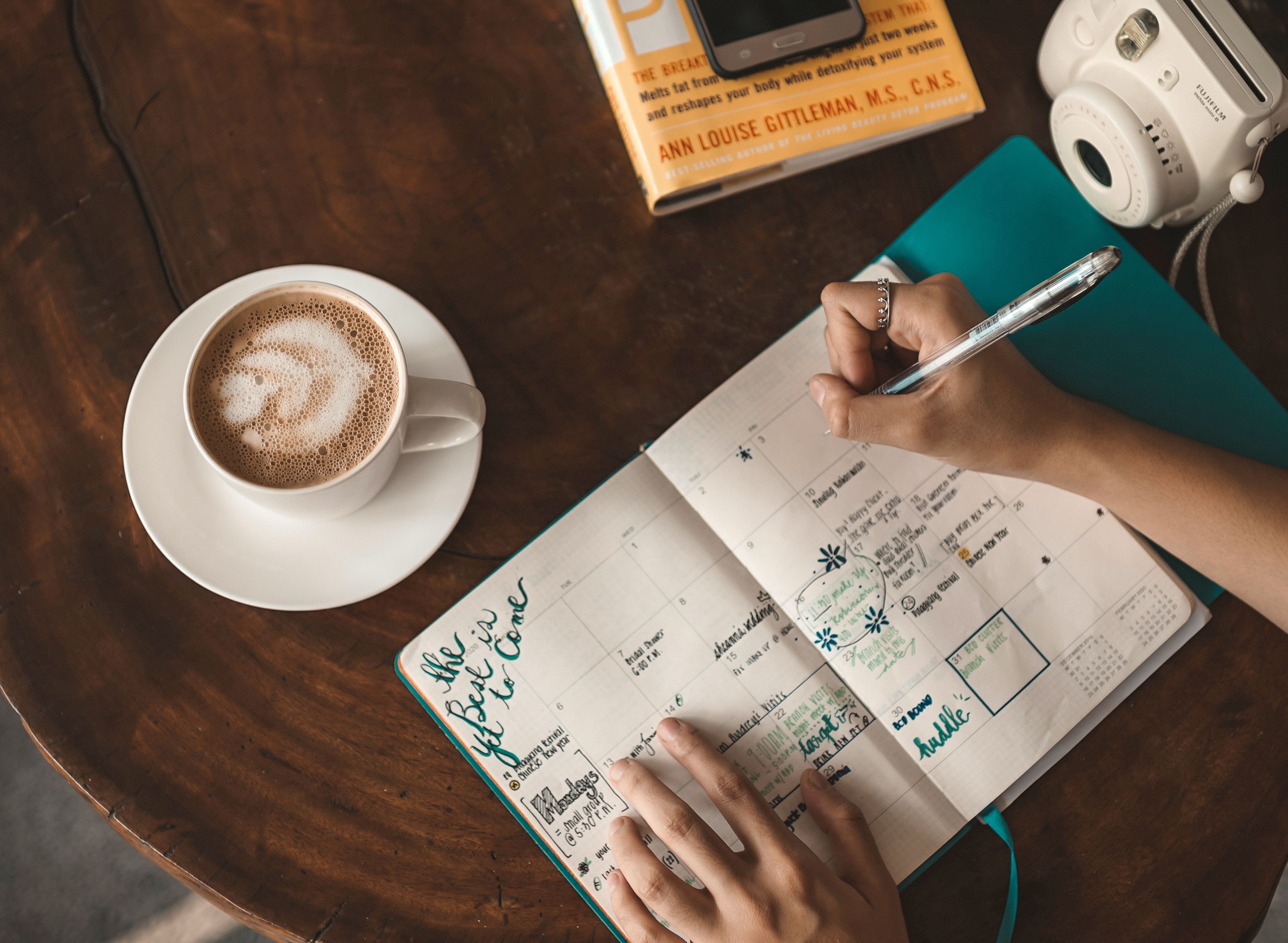 Person journaling with a cup of chai on a wooden desk in morning light
