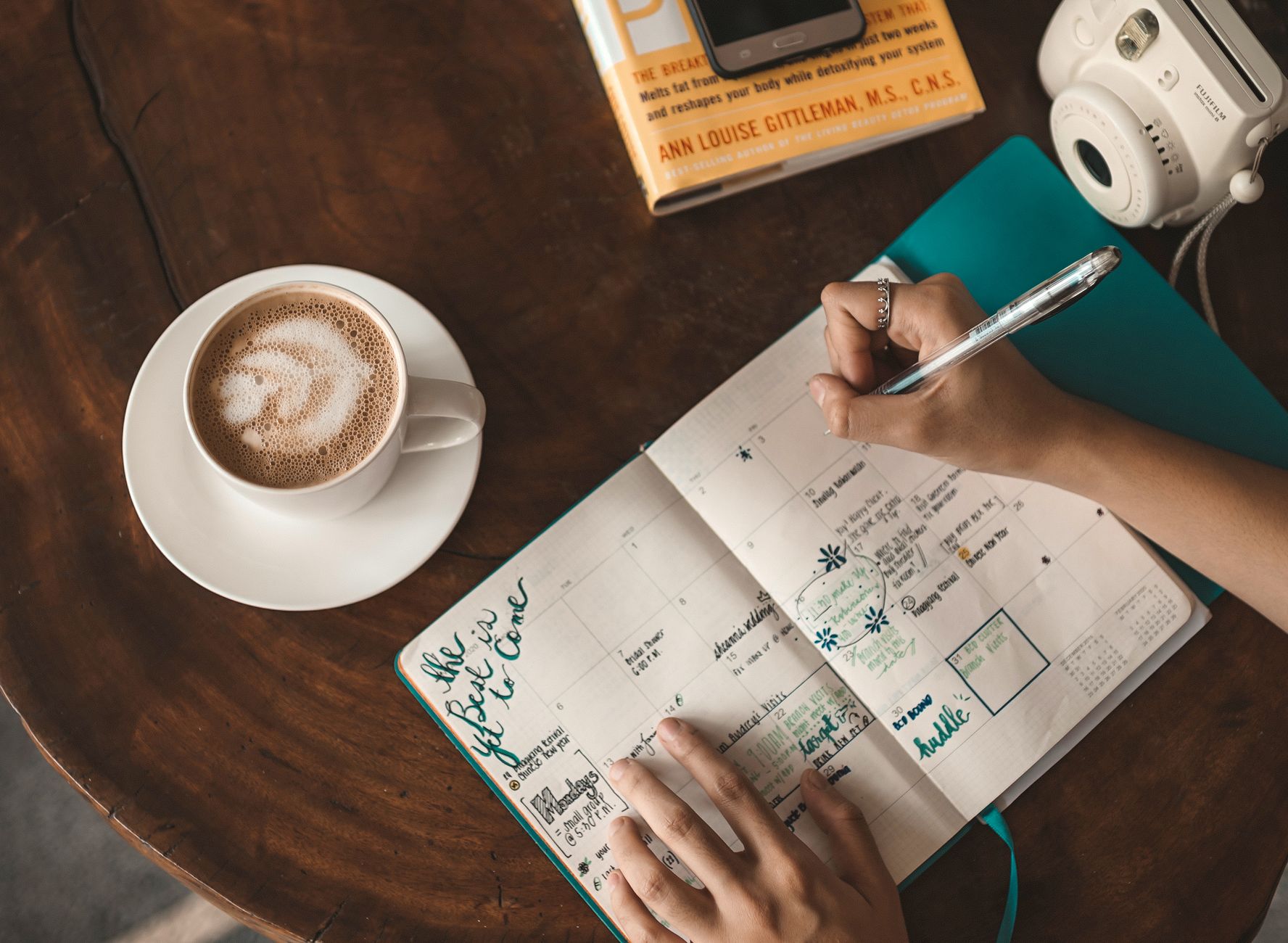 Person journaling with a cup of chai on a wooden desk in morning light