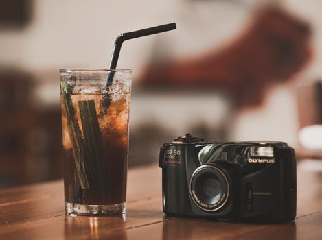 Glass of iced drink with a camera on a wooden table. Cozy indoor setting.