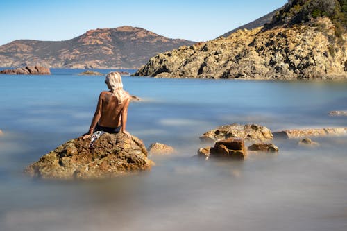 Blonde Woman Sitting Topless on Rocks on Sea Shore
