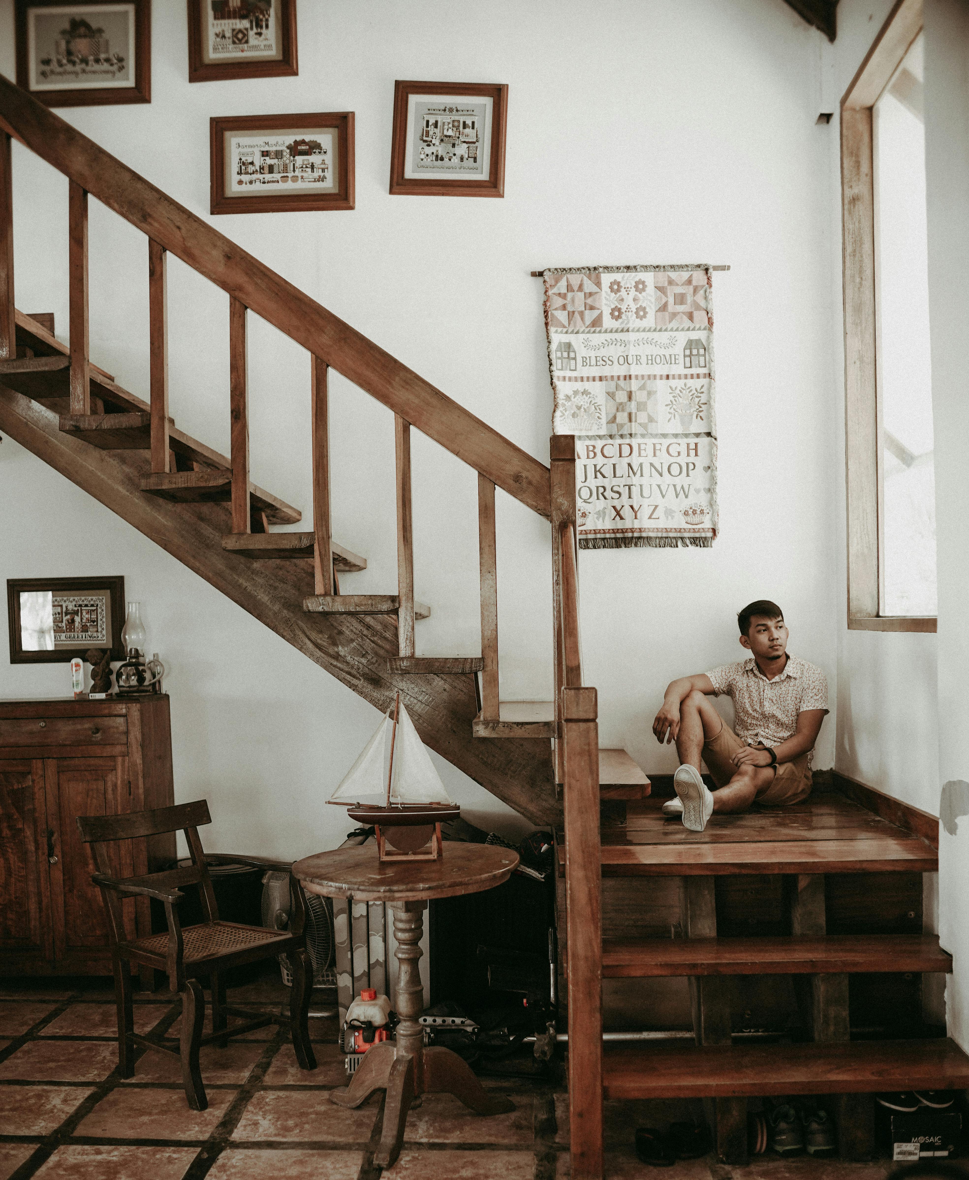 Free A man sits thoughtfully on rustic wooden steps in a cozy interior setting. Stock Photo