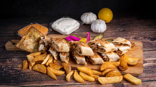 A mouth-watering display of shawarma, fries, sauces, and pickles on a rustic table.