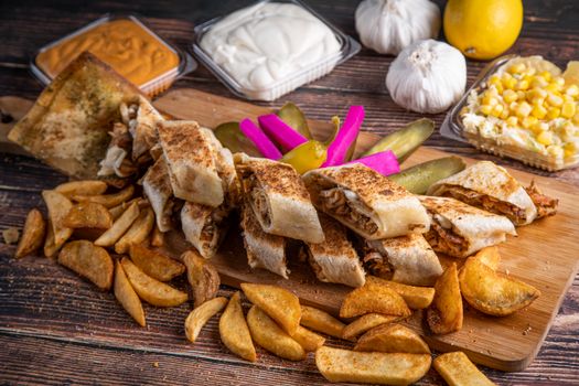 Savory shawarma wrap served with crispy fries, pickles, and sauces on a rustic wooden board.