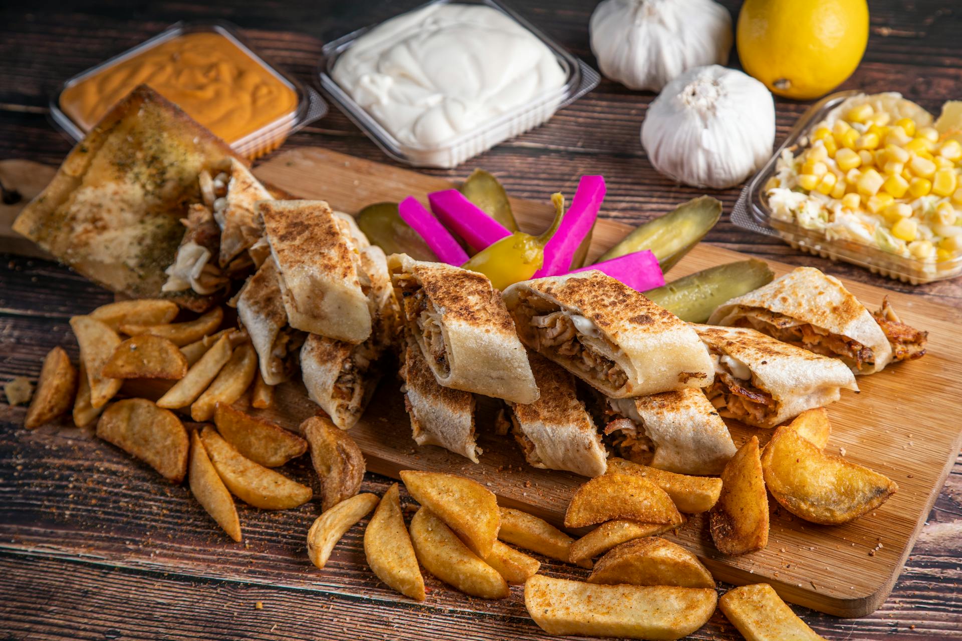 Savory shawarma wrap served with crispy fries, pickles, and sauces on a rustic wooden board.
