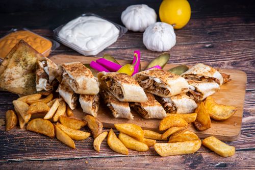 Free Mouth-watering shawarma wraps with crispy fries and flavorful dips on a rustic wooden board. Stock Photo
