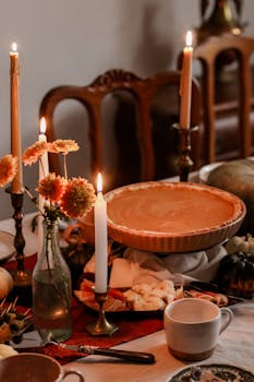 Warm autumn table setting with pumpkin pie, candles, and fall decor, creating a cozy ambiance.
