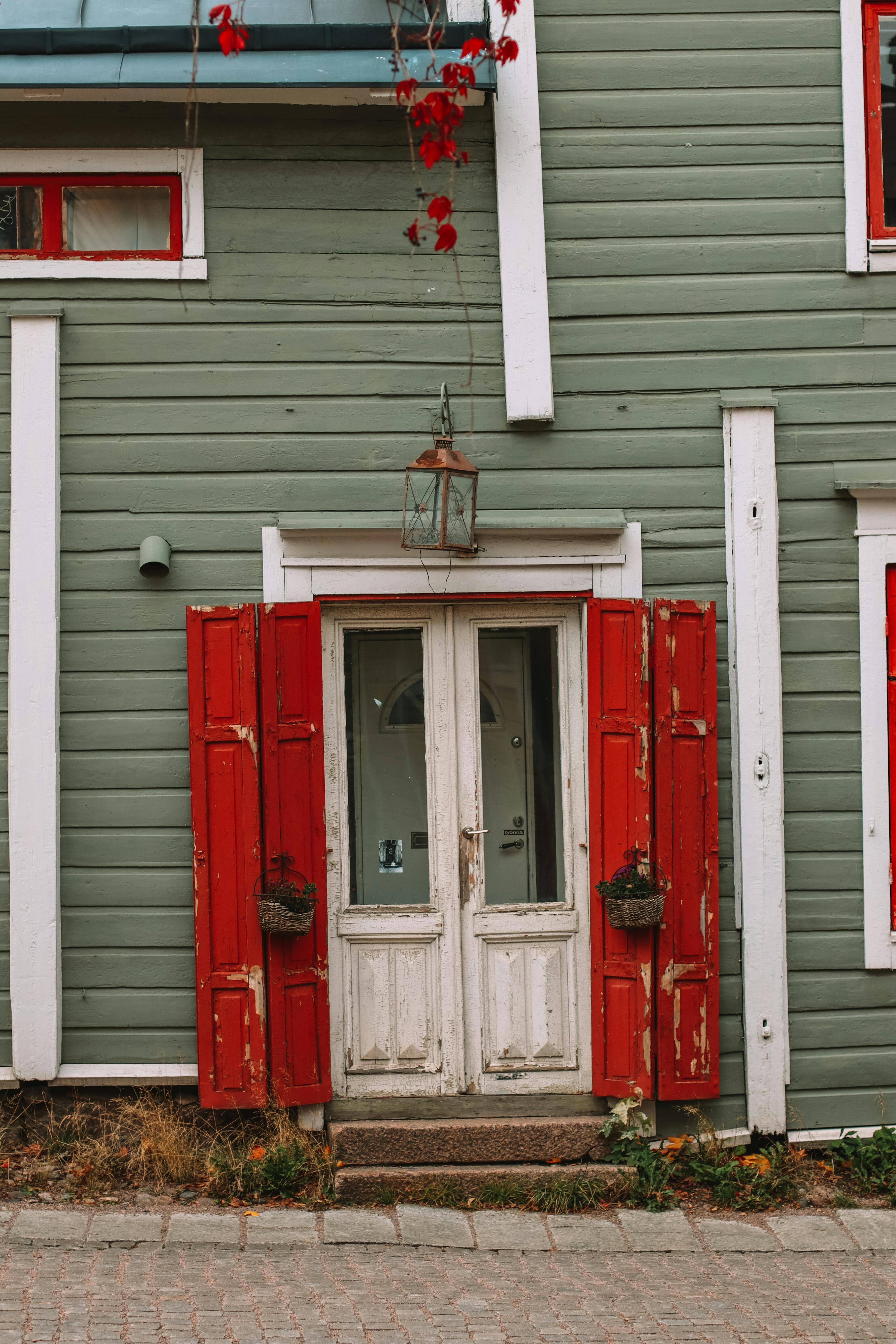 A charming wooden house façade featuring red shutters and a vintage lantern.