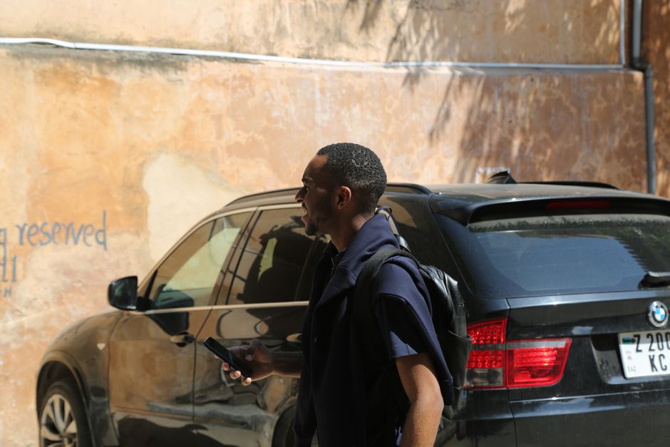 African American man using smartphone while walking by parked BMW in city area.