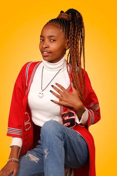 Confident woman wearing trendy red jacket posing in studio with a bright yellow background.