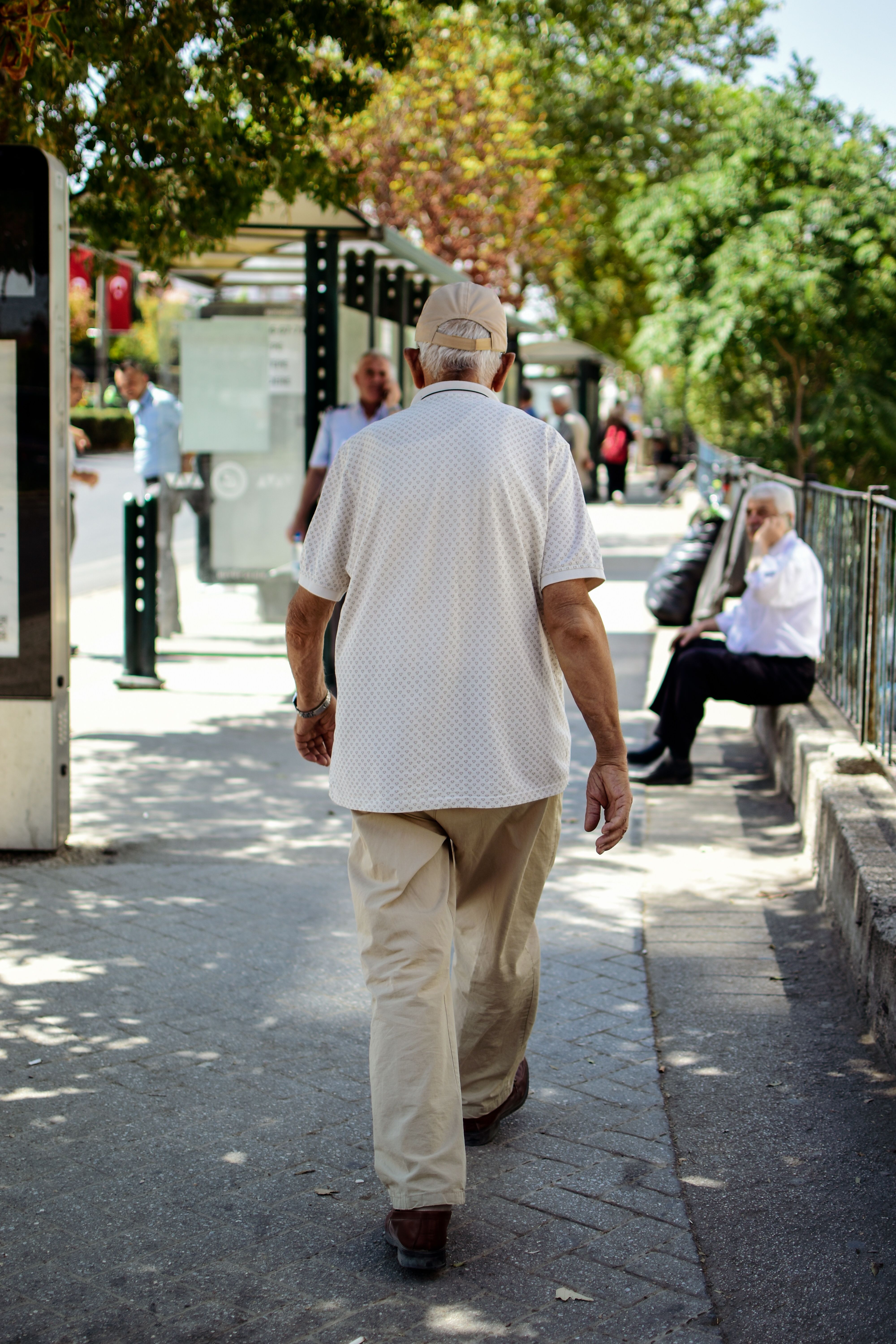 Back view of a senior man walking on a city sidewalk on a sunny day.