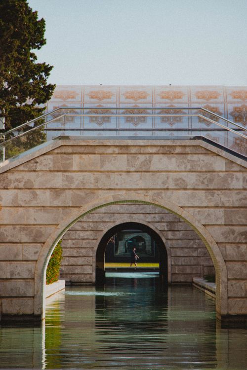 Free Stone bridge gracefully arches over a tranquil canal, reflecting architecture's beauty. Stock Photo
