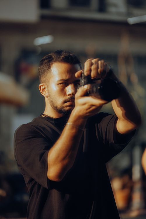 Free A man with short hair using a camera outdoors, in a candid moment of concentration. Stock Photo