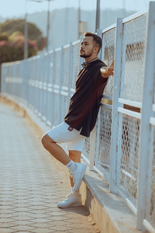 Free Stylish man in black t-shirt and white shorts relaxing outdoors, displaying modern fashion. Stock Photo