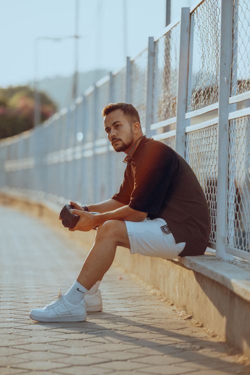 Free Male photographer relaxing on a sunny urban bridge, holding a camera. Stock Photo