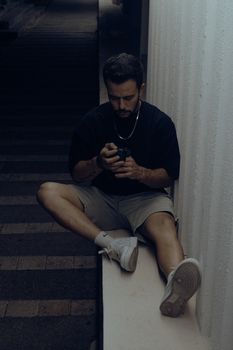 A man sitting in an urban setting using his smartphone at night, portraying solitude and concentration.