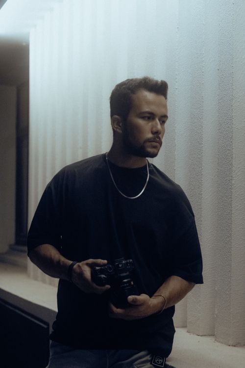 Free A young man with a black t-shirt and short hair holding a camera outdoors at night. Stock Photo