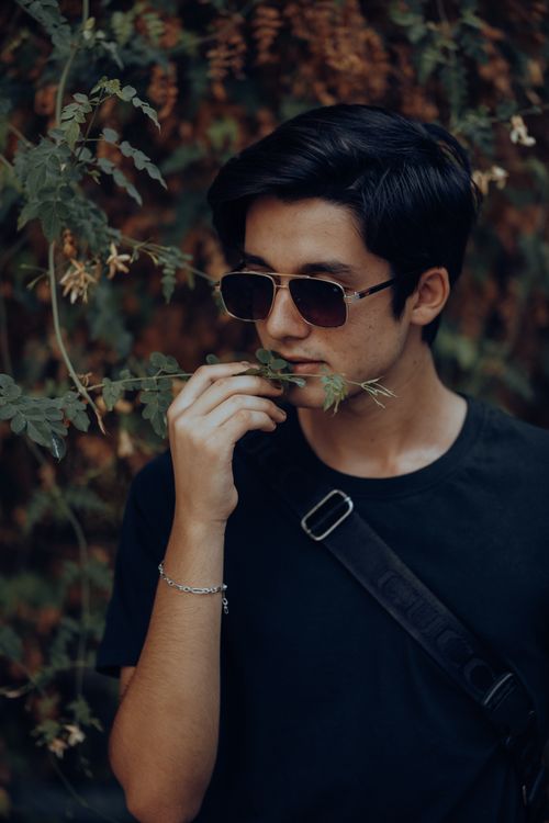 Free Close-up of a young man wearing sunglasses, contemplating in a leafy setting. Stock Photo