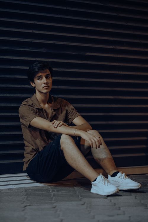 Free A young man sits against a dark urban backdrop, embodying a relaxed street style. Stock Photo