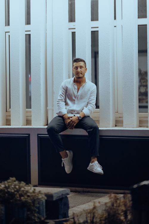 Free A stylish man in casual attire sitting on an urban structure, captured at night. Stock Photo