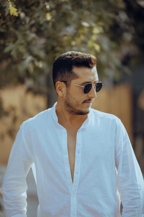 Free Portrait of a fashionable man in a white shirt and sunglasses, enjoying a sunny day outdoors. Stock Photo